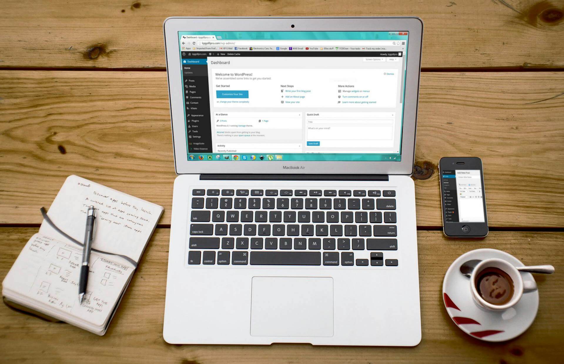 Anteckningsbok, kaffe, mobil och en laptop med WordPress startsida på skärmen
