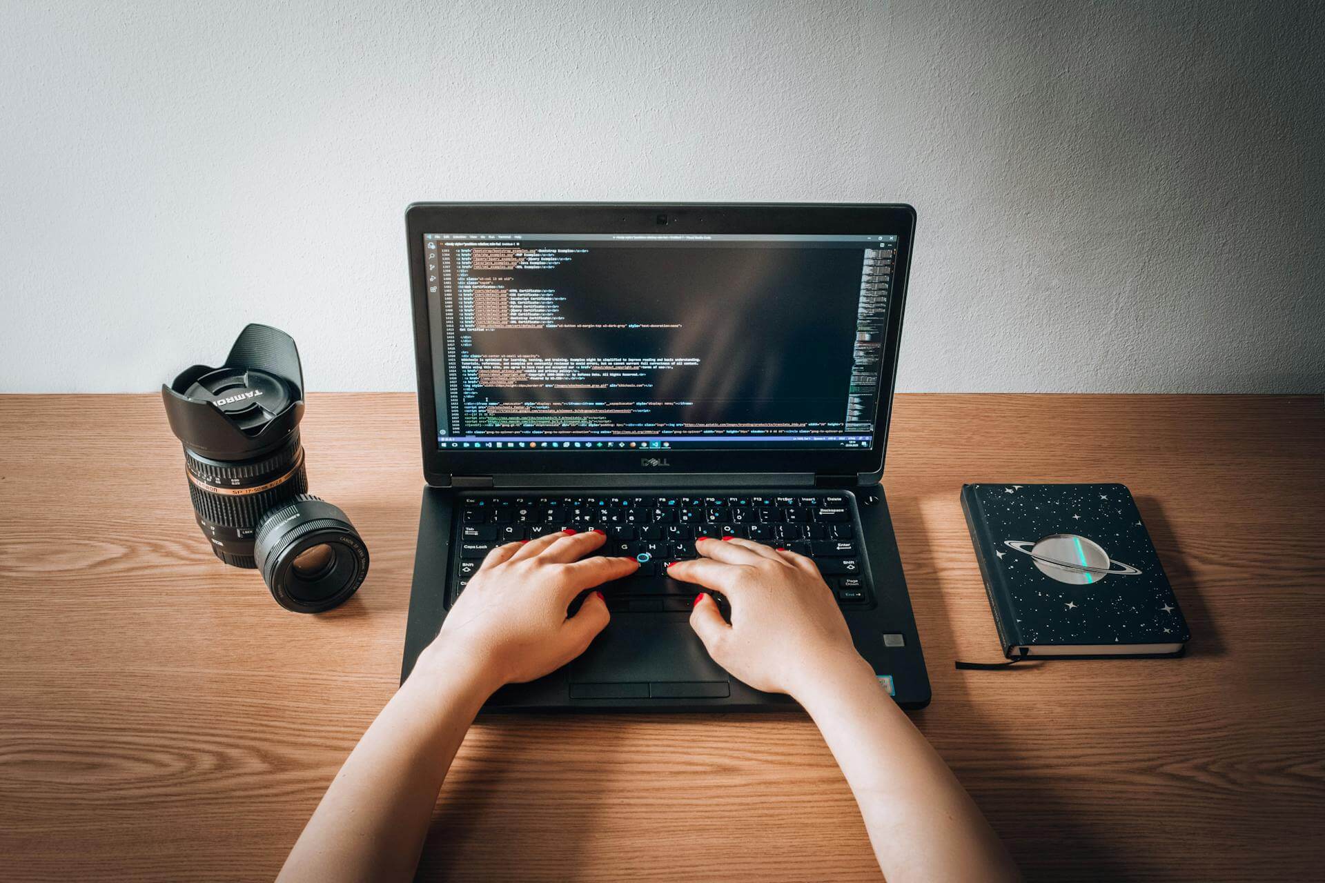 En personvid ett skrivbord med en kamera, en bok och en laptop som jobbar med html