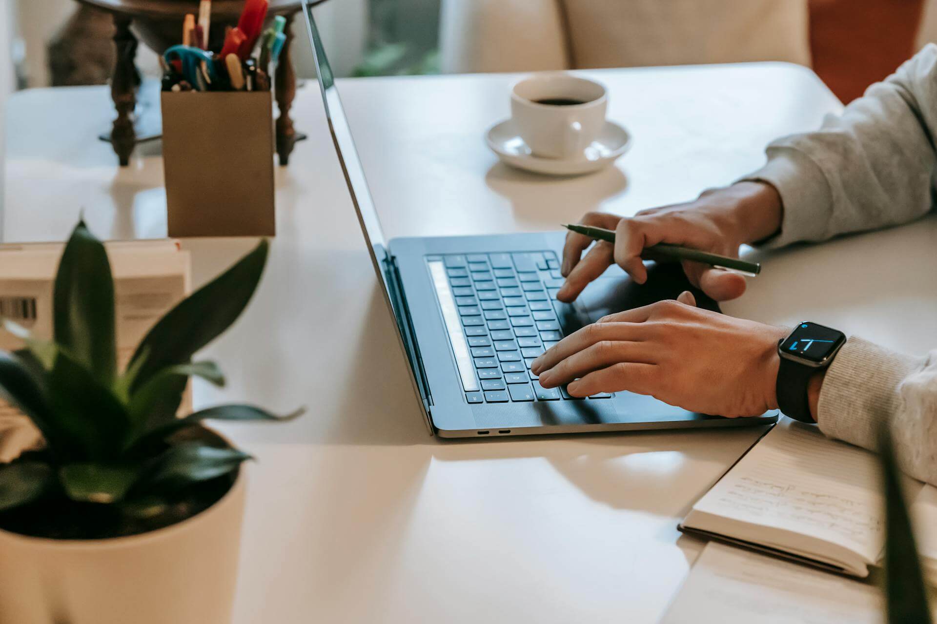 En person vid sitt skrivbord med en penna i handen som jobbar framför sin laptop