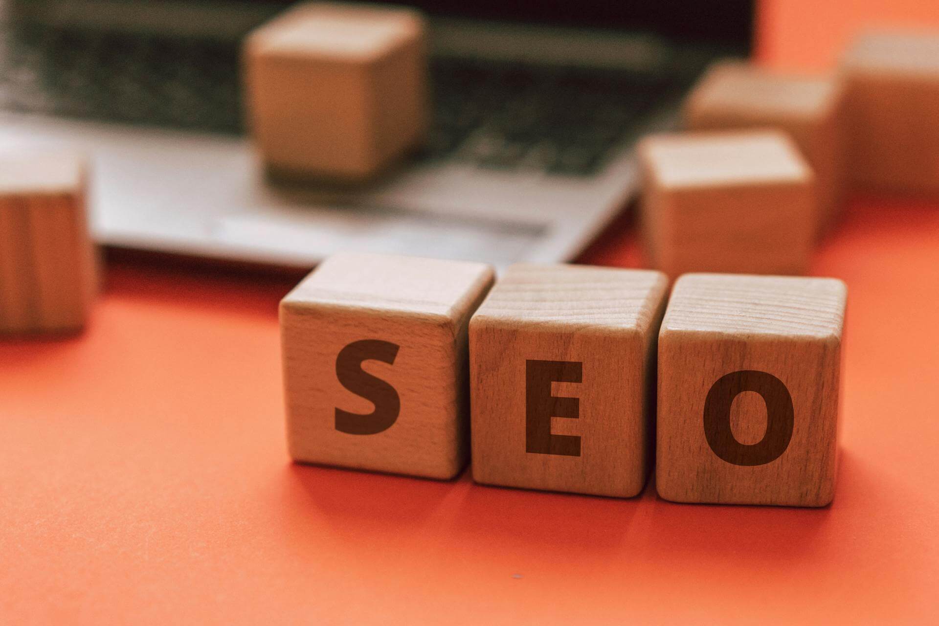 Träkuber med bokstäver på som stavar SEO med en laptop i bakgrunden
