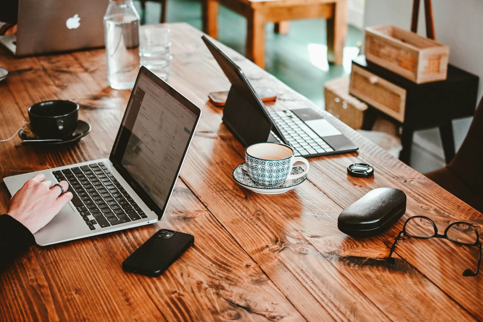Person som sitter vid ett stort bord med kaffe, mobil, glasögon och flera datorer, representerar en webbyrå som arbetar med WordPress